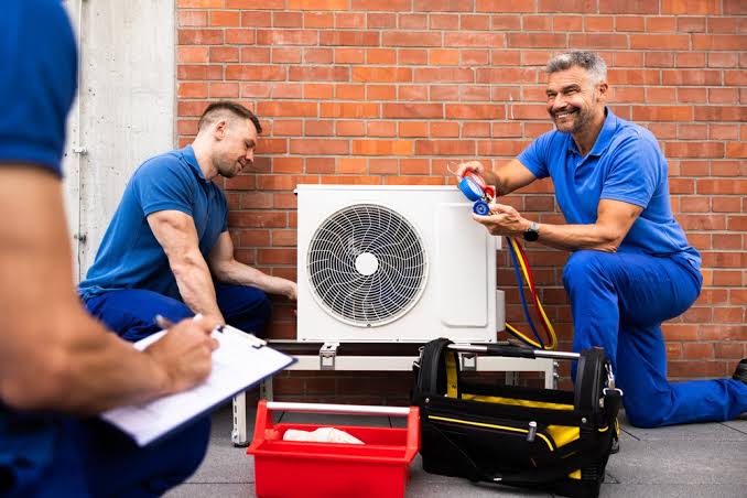 HVAC technicians inspecting an outdoor air conditioning system beside a brick wall